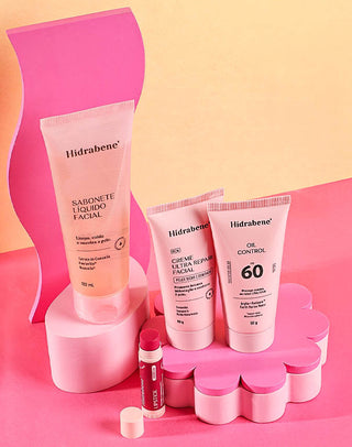 Produtos Hidrabene em cenário rosa: sabonete líquido facial, creme ultra repair facial, protetor solar oil control FPS 60 e lipstick