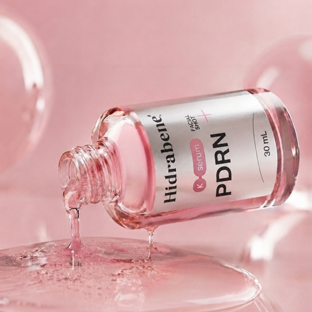 Modelo pingando o sérum na bochecha com o conta-gotas, segurando o frasco