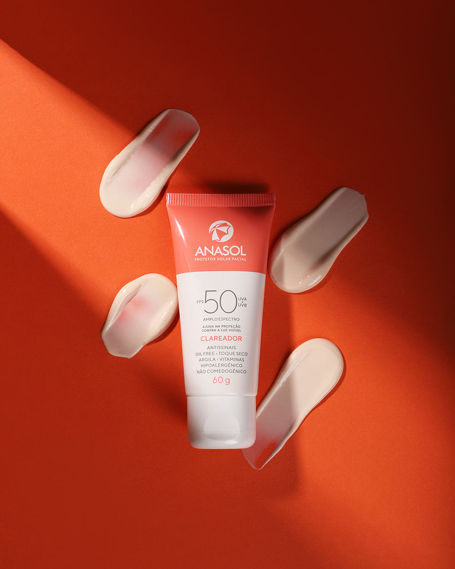 A bisnaga do Clareador FPS 50 deitada sobre fundo laranja, cercada de quatro riscos de creme.