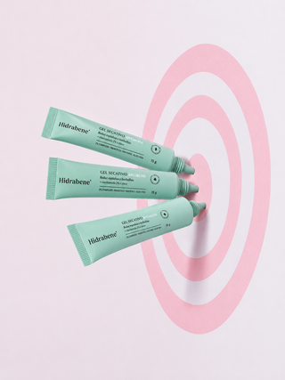 Três bisnagas do Gel Secativo Antiacne Hidrabene apontadas para o centro de um alvo rosa