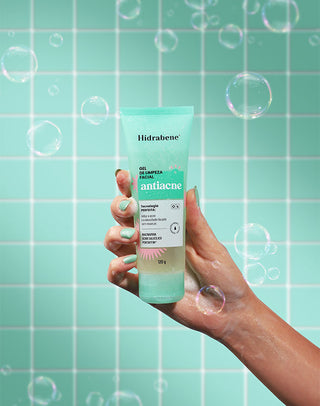 Mão segurando o Gel de Limpeza Facial Antiacne Hidrabene em fundo de azulejos verdes