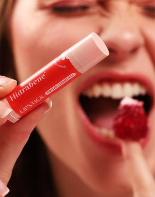 Modelo segurando o Lipstick Frutas Vermelhas Hidrabene antes de morder uma framboesa