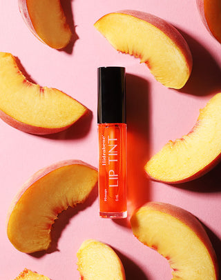 Lip Tint Pêssego Hidrabene cercado de fatias de pêssego em fundo rosa