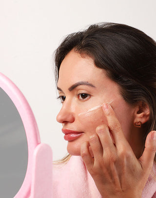 Mulher aplicando o creme Retinol Noturno Hidrabene no rosto em frente ao espelho