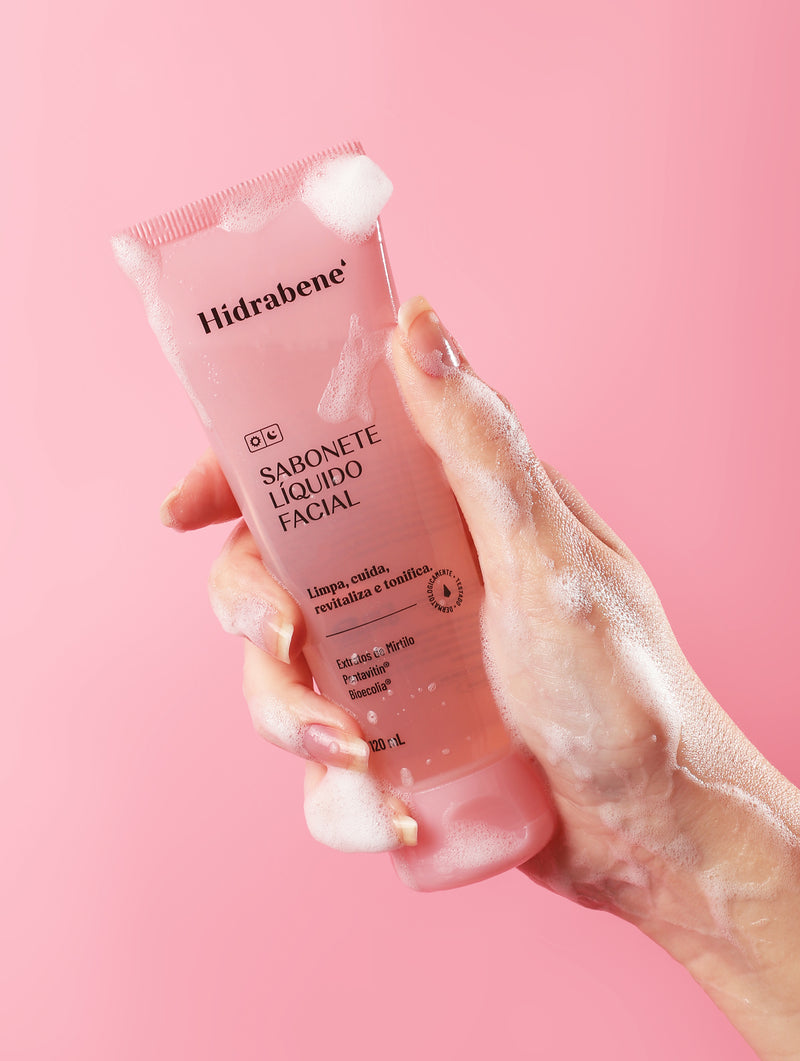 Mão com espuma segurando o Sabonete Líquido Facial Hidrabene em fundo rosa