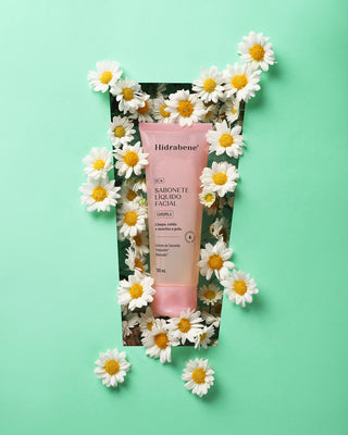 Sabonete Líquido Facial Camomila Hidrabene cercado por flores de camomila em fundo verde-água