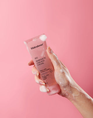 Mão com espuma segurando o Sabonete Líquido Facial Hidrabene em fundo rosa