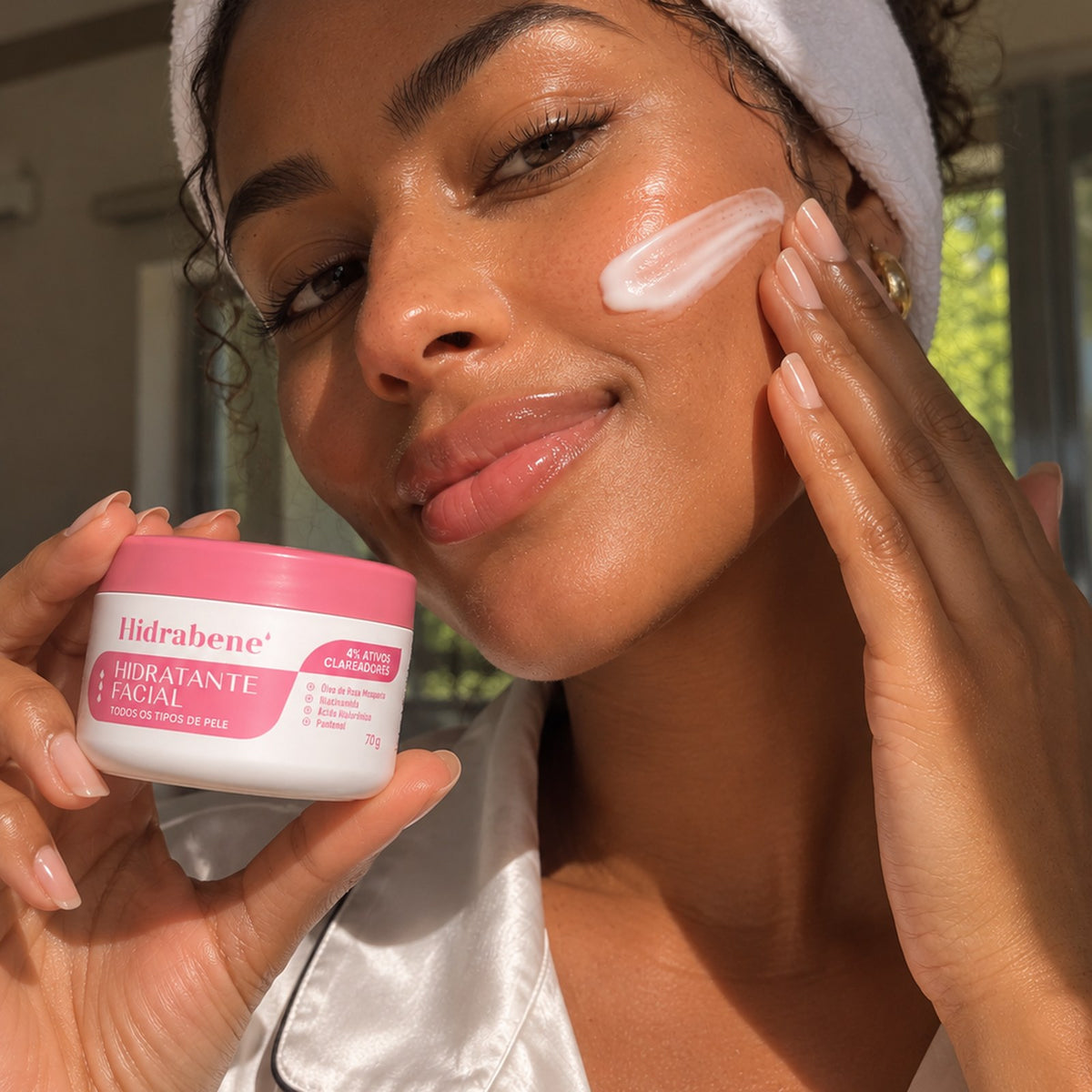 Mulher aplicando o hidratante facial no rosto, com o pote na mão.