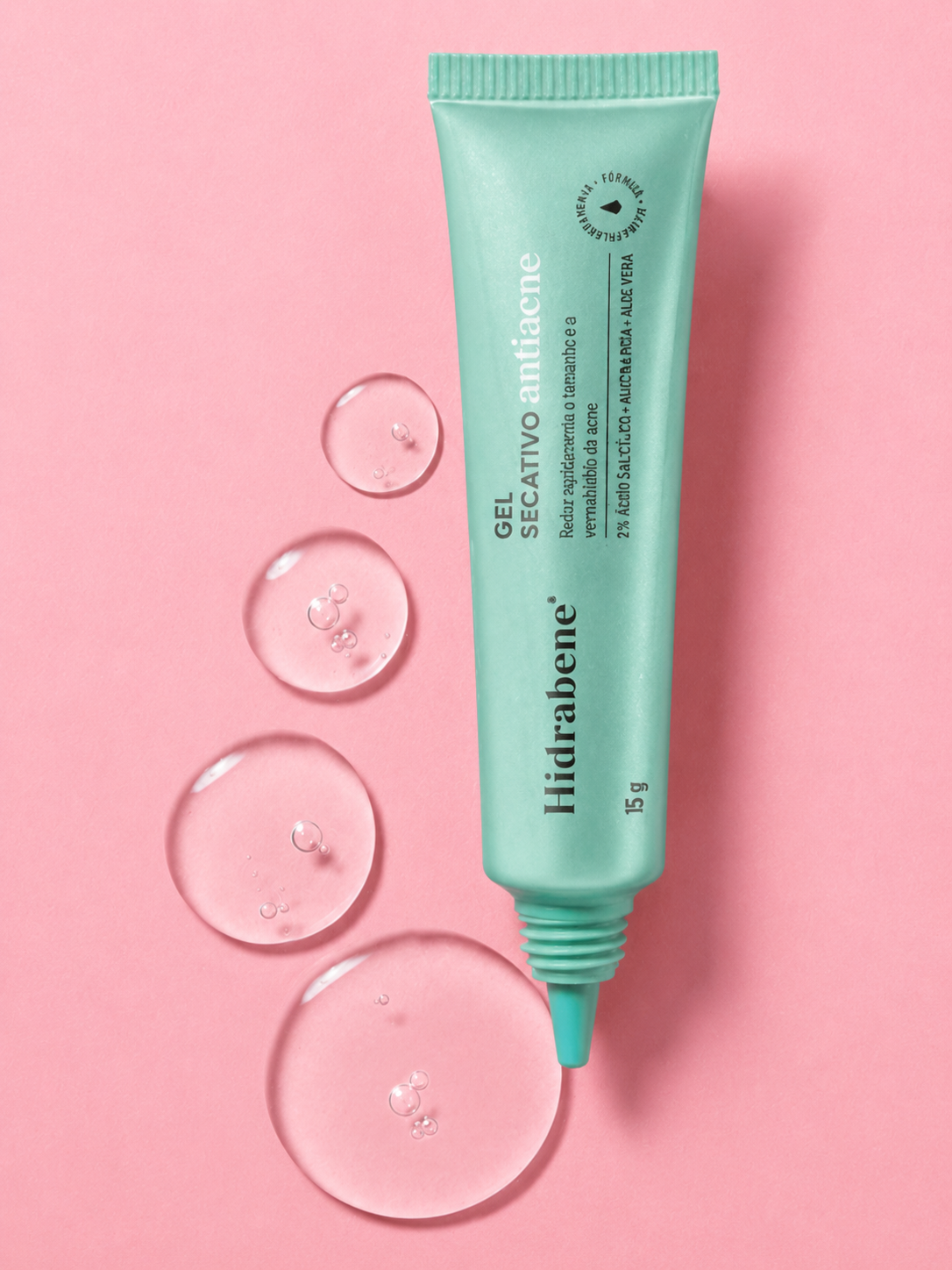 Bisnaga do Gel Secativo Antiacne Hidrabene sobre fundo rosa com gotas de gel