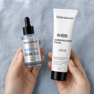 Mãos segurando o Sérum GHK-Cu e o Harmonizador Facial sobre linho azul-acinzentado