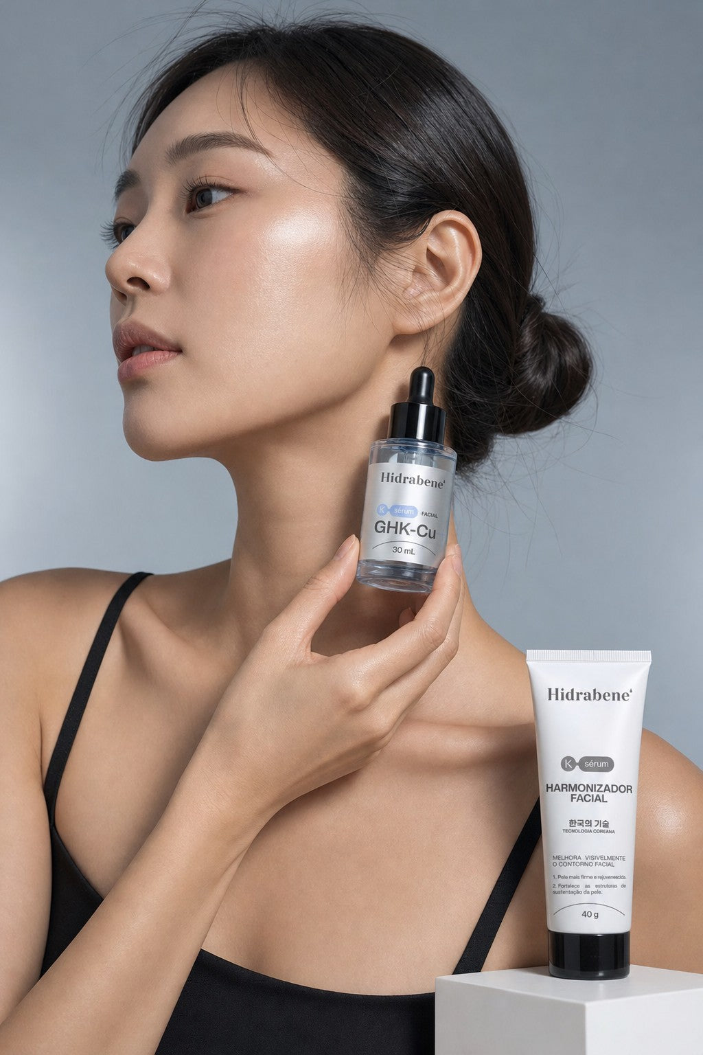 Mulher de perfil segurando o Sérum GHK-Cu perto do maxilar, com o Harmonizador Facial ao lado